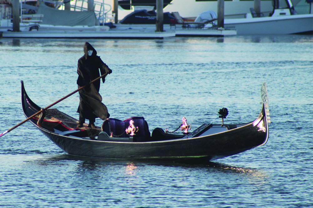 Masked figure rowing a gondola on calm water in san diego