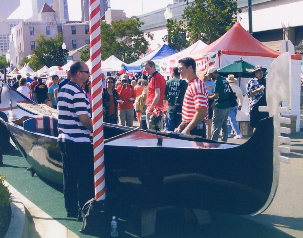 Elegant black Venetian gondola on display at an Italian festival with red carpet and Venice-themed backdrop, perfect for event décor or photo opportunities.