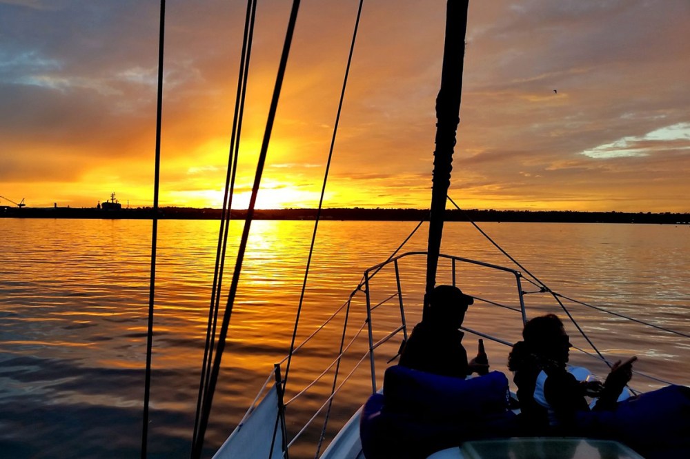 Couple sitting on the bow of a sailboat during a sunset cruise in San Diego