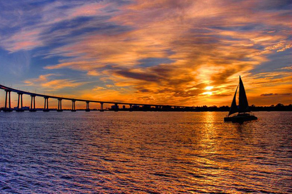 Sailboat cruising at sunset with the Coronado Bridge over San Diego Bay.