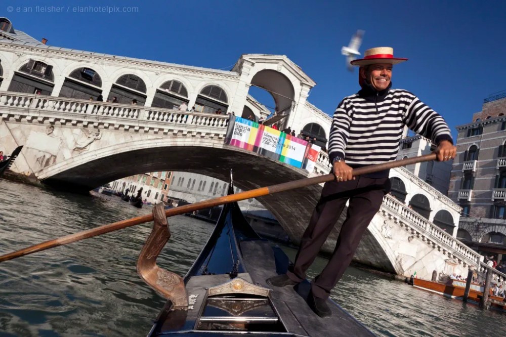 Smiling gondolier rowing in Venice in stripes and hat