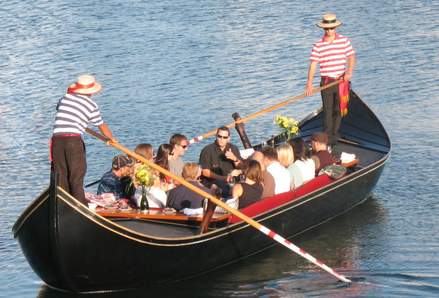 large Venetian gondola with two gondoliers holding a group celebration on sunny San Diego waterway